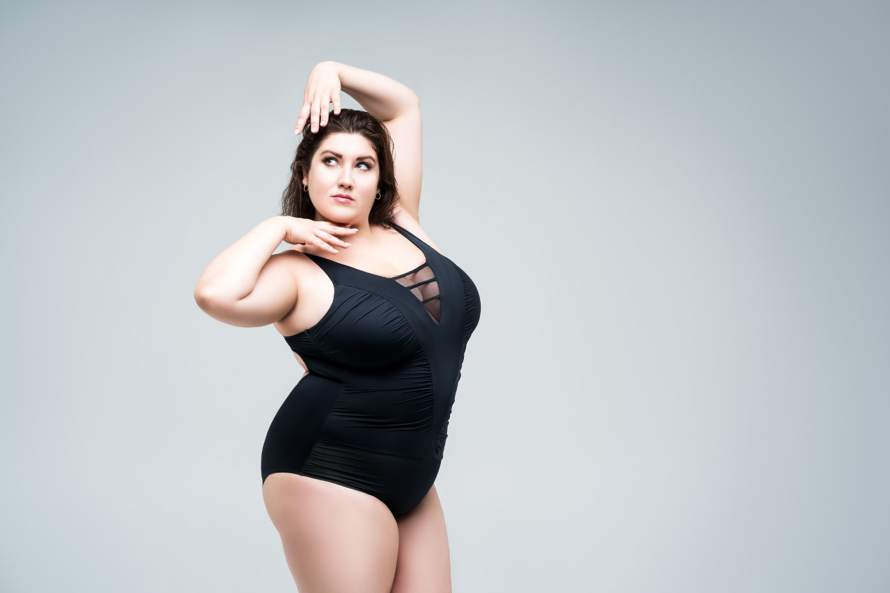 Sexy plus size fashion model in black one-piece swimsuit, woman in lingerie on gray background
